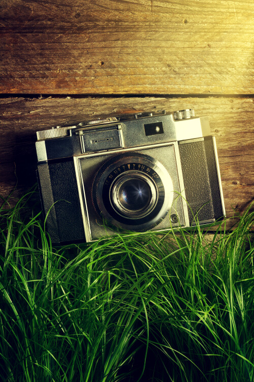 old-vintage-camera-green-grass-with-light-beams-wooden-background-top-view.jpg